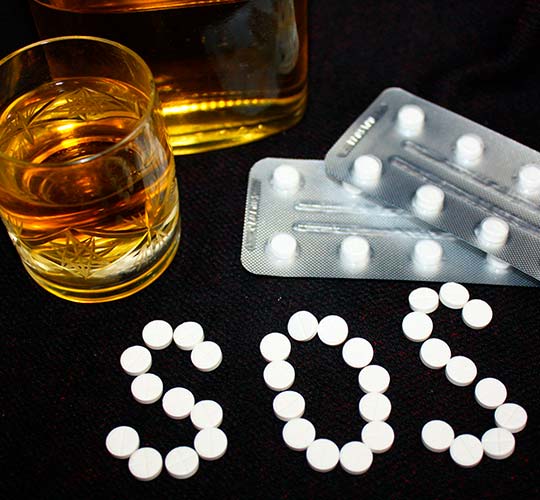 стакан с алкоголем и таблетки на столе