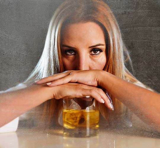 женщина положила руки на стакан с алкоголем и смотрит в камеру